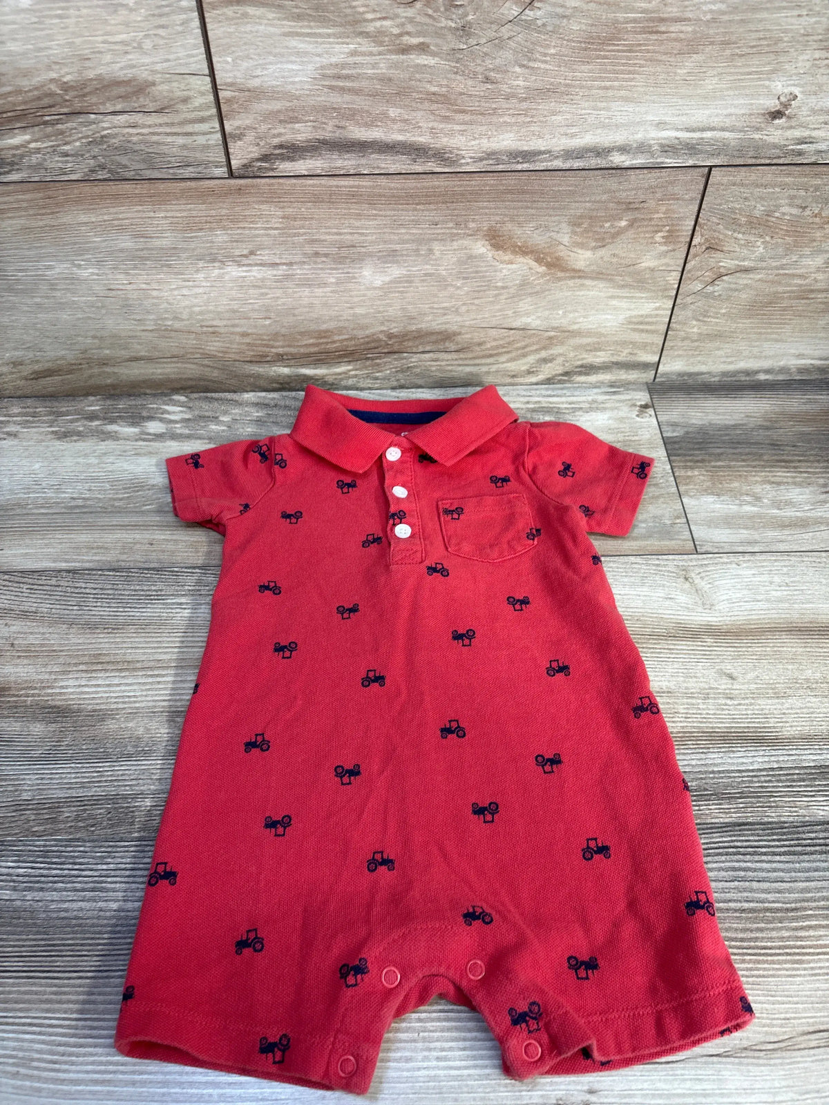 Front view of Carter’s red polo shortie romper showcasing navy tractor print, collar, buttons, and chest pocket