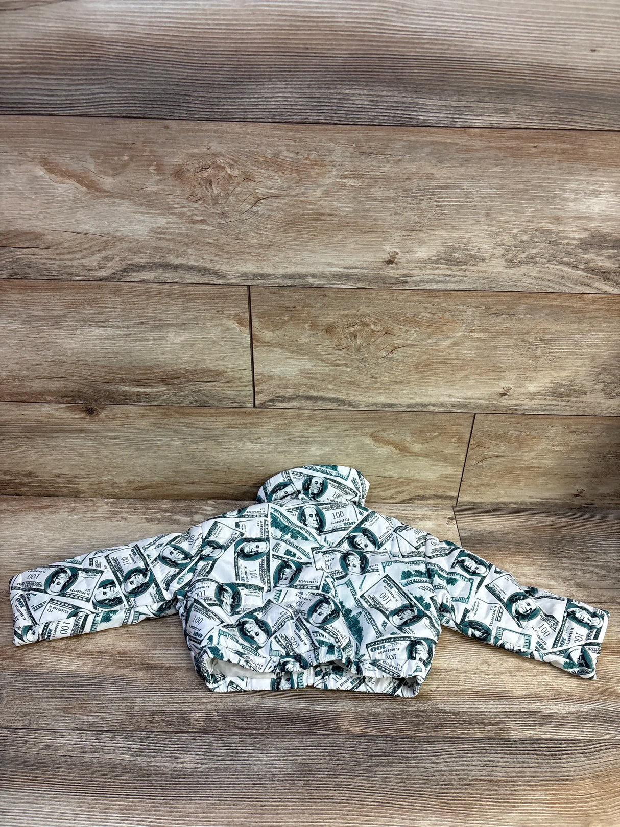 Back view of Shein toddler white puffer jacket showing green money-bill print, elasticated hem and high collar on wood background