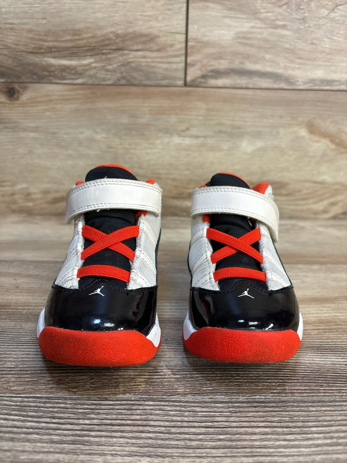 Front view of Air Jordan 6 Rings TD toddler sneakers (sz 10C) showcasing velcro strap closure, black patent toe, and red outsole on wood floor