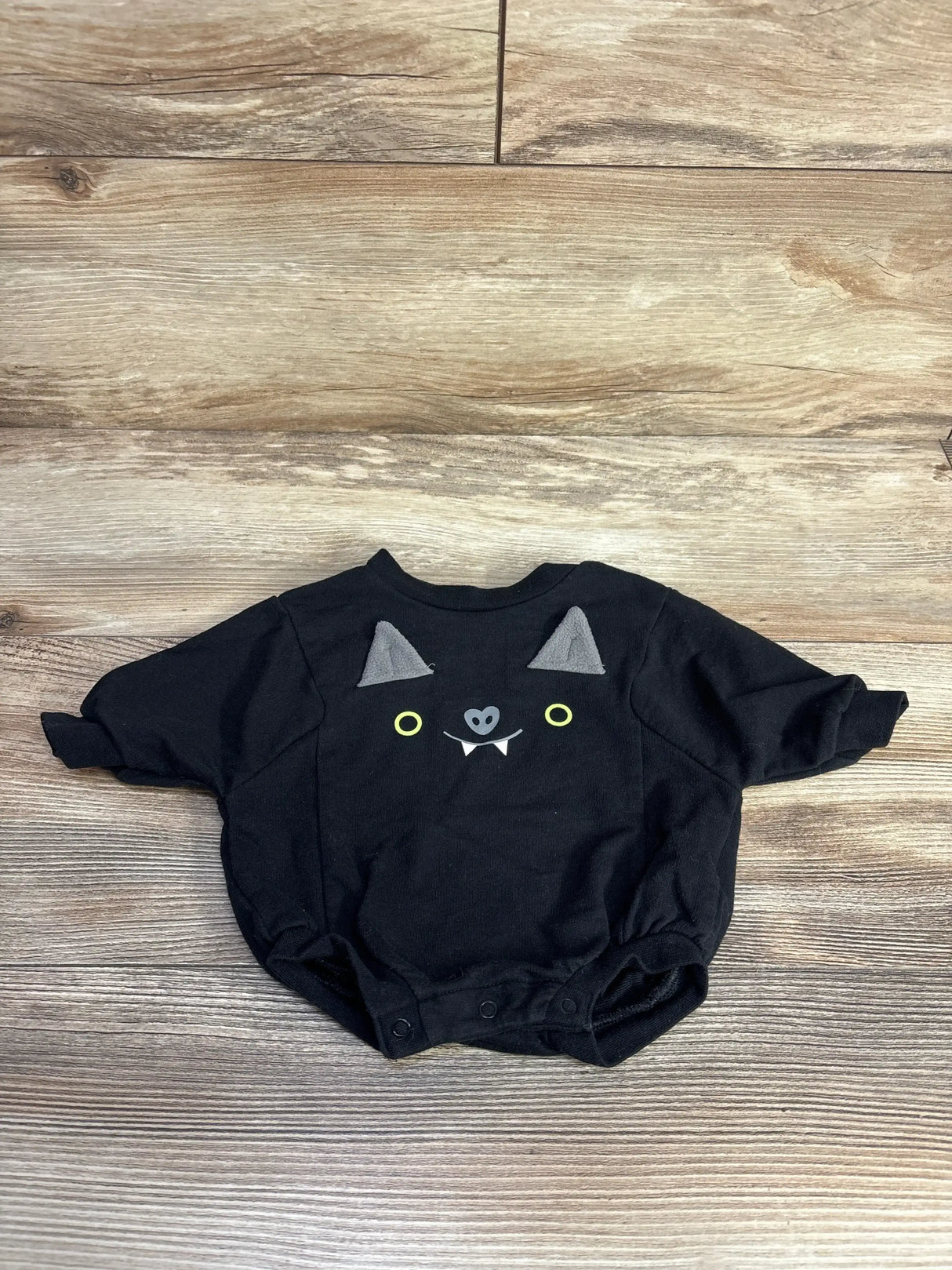 Front view of newborn black Cat and Jack bat romper with bat face, felt ears, and snap crotch on wood floor background