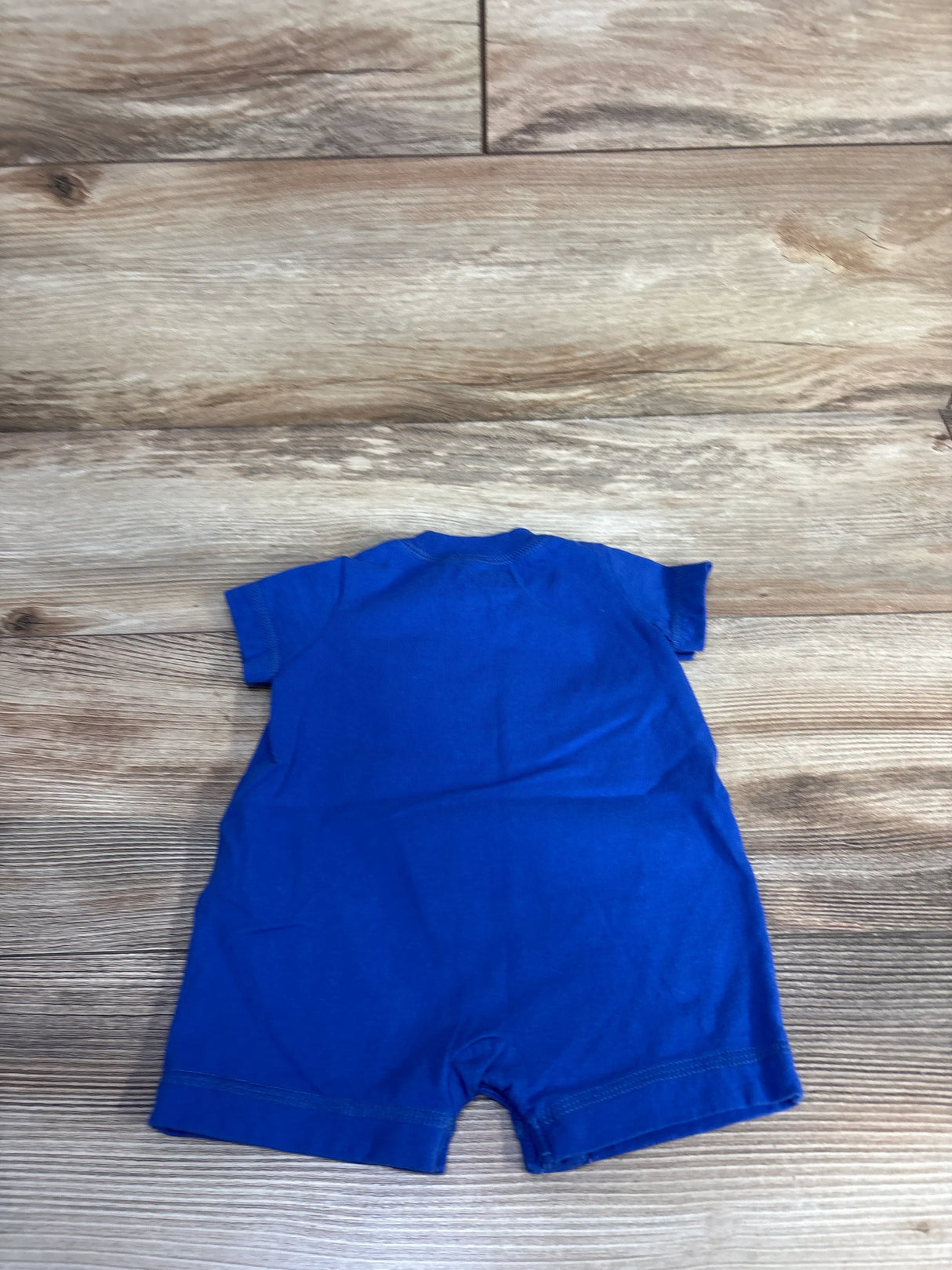 Back view of Carter’s Whale shortie romper in bright blue showing short sleeves and short legs on wood plank background