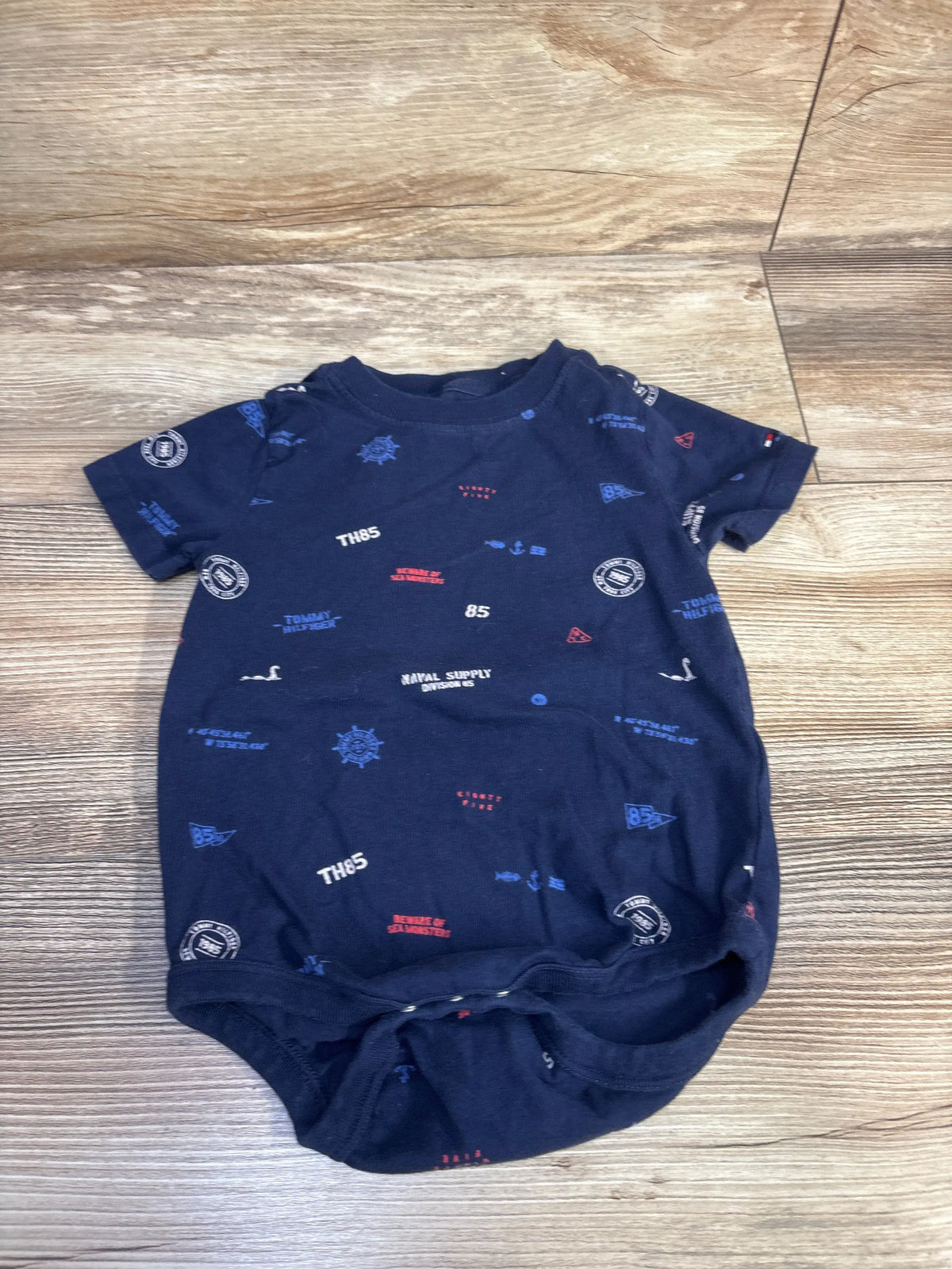 Front view of Tommy Hilfiger Bodysuit Navy sz 24m showcasing allover nautical print and bottom snaps on wood floor