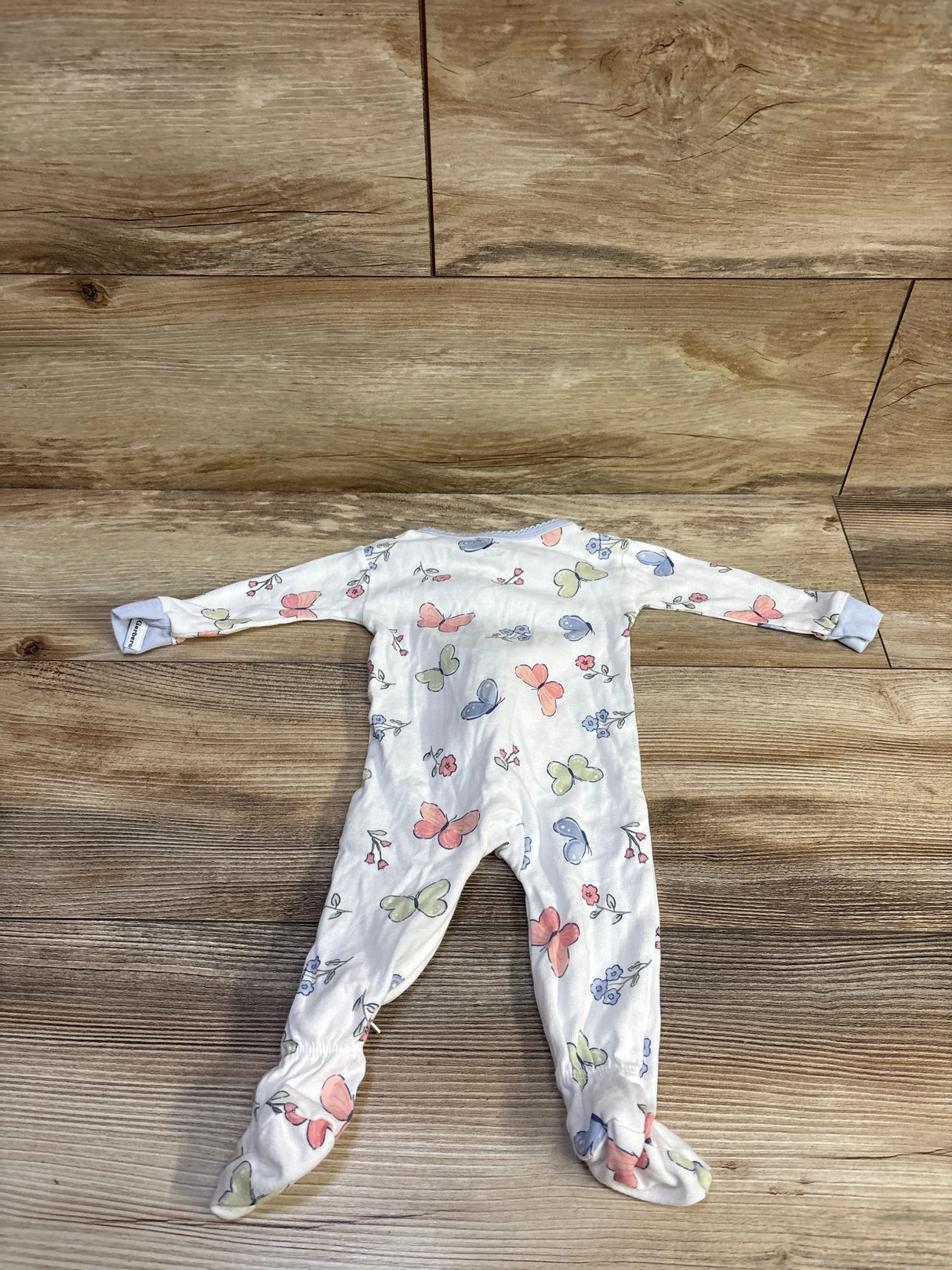 Flat lay of Gerber white long-sleeve footed sleeper showcasing pastel butterfly print on wood floor background