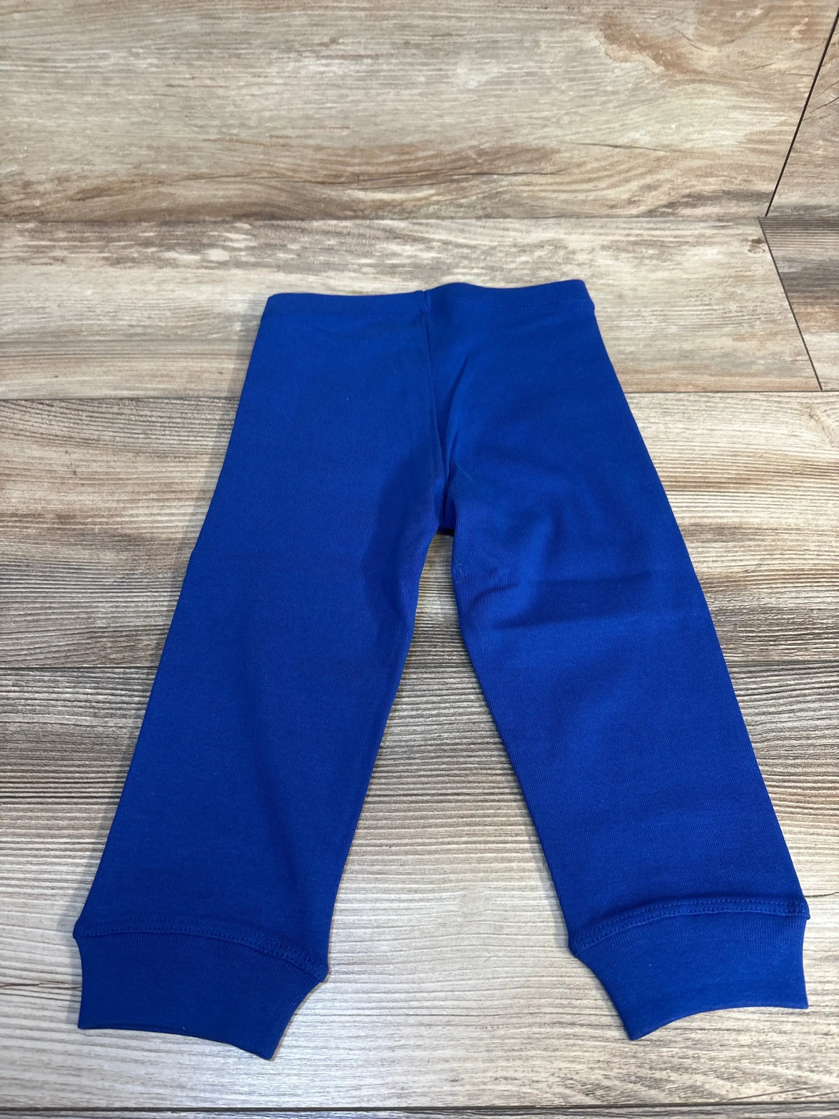 Top-down view of NEW Primary Leggings in blue, size 12-18 months, showcasing elastic waistband and ankle cuffs on a wood background