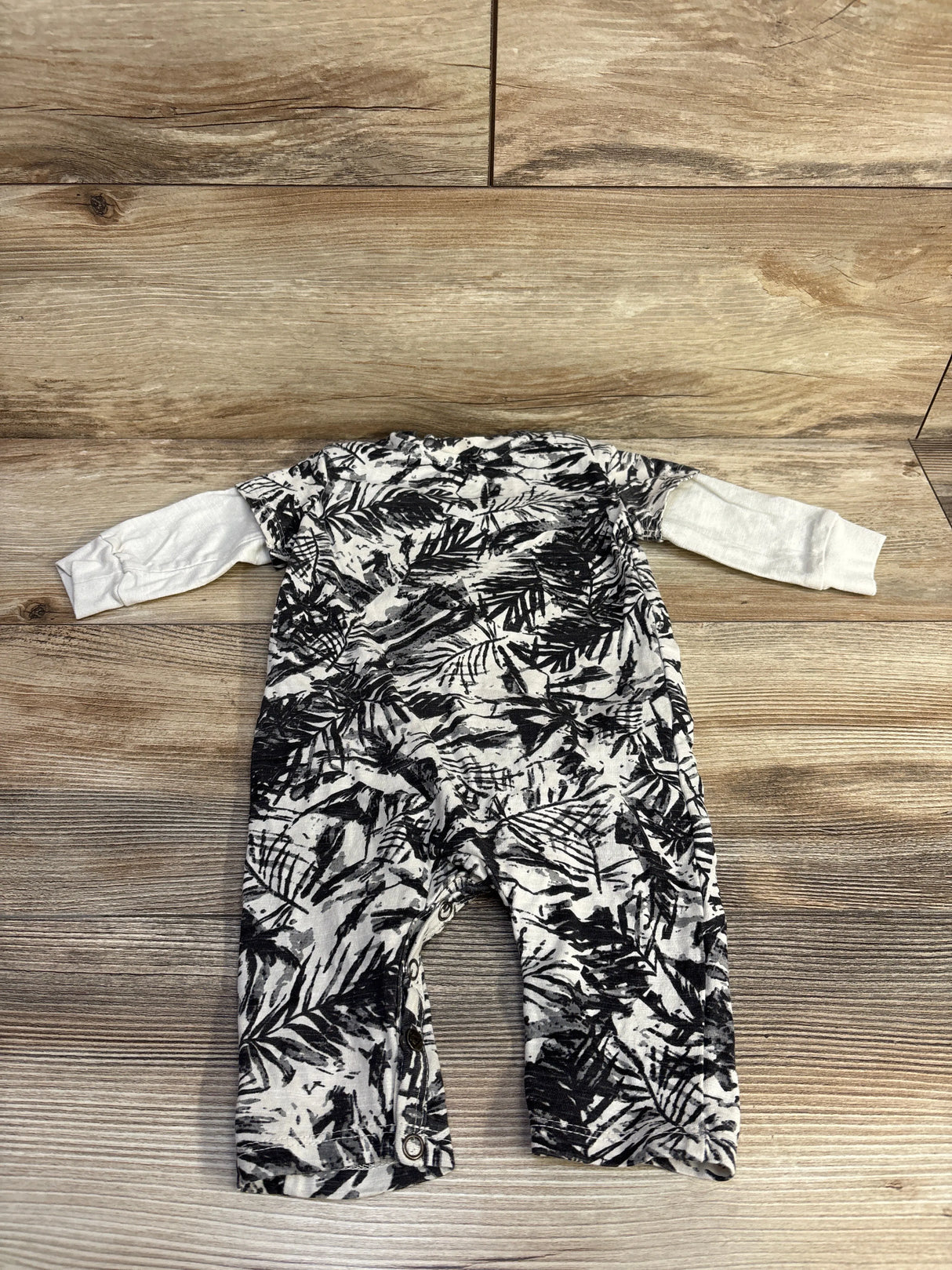 Black and white baby romper with leaf print on wood floor