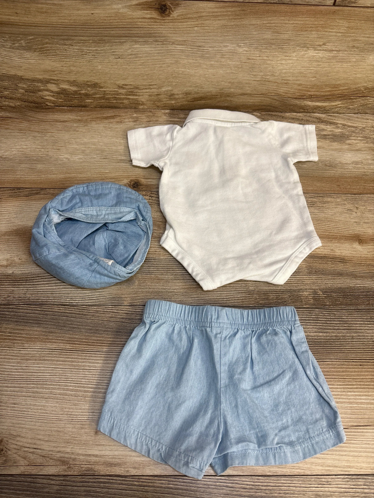 Baby boy's outfit with white bodysuit, light blue shorts, and matching blue hat on wood background