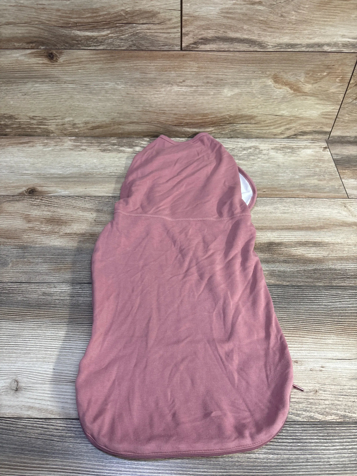 Top view of Momcozy bamboo swaddle wrap in pink, size 0 to 3 months, showing its hood and side ties on a wood-look floor