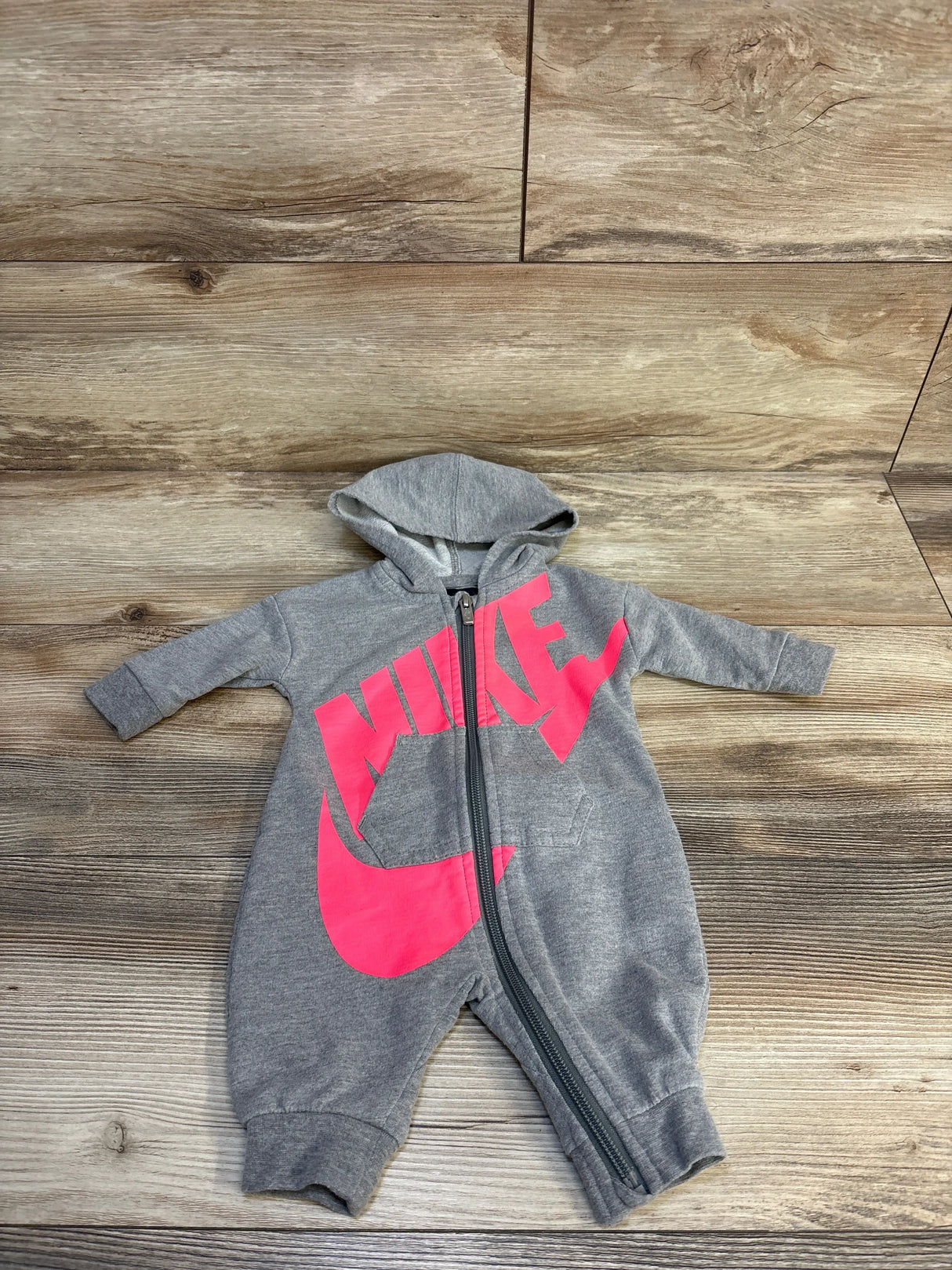 Gray hooded baby romper with pink logo and zipper front on wood background