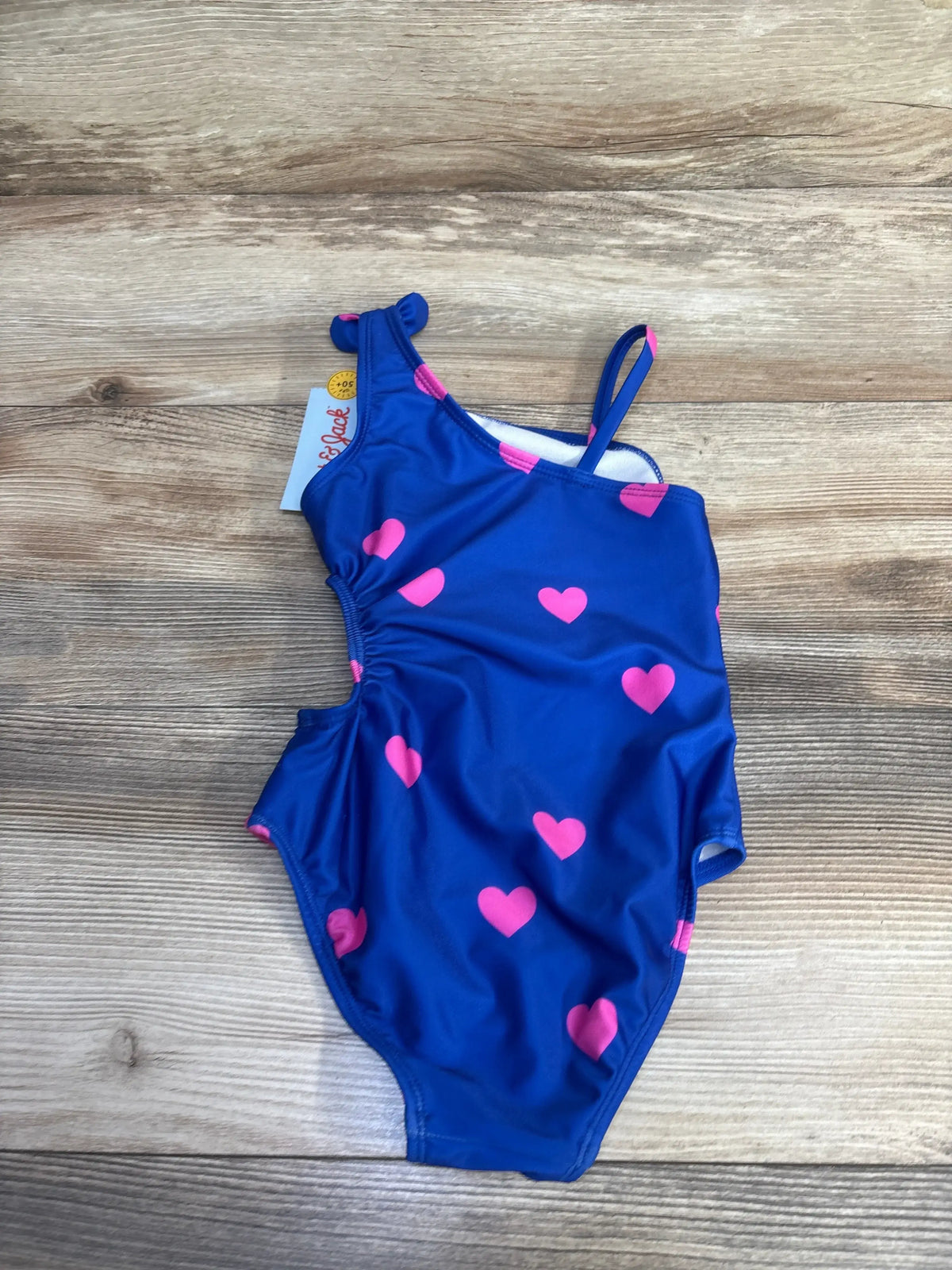 Front view of Cat & Jack blue one-piece cut-out swimsuit with pink heart pattern and thin shoulder straps on a wood-grain background
