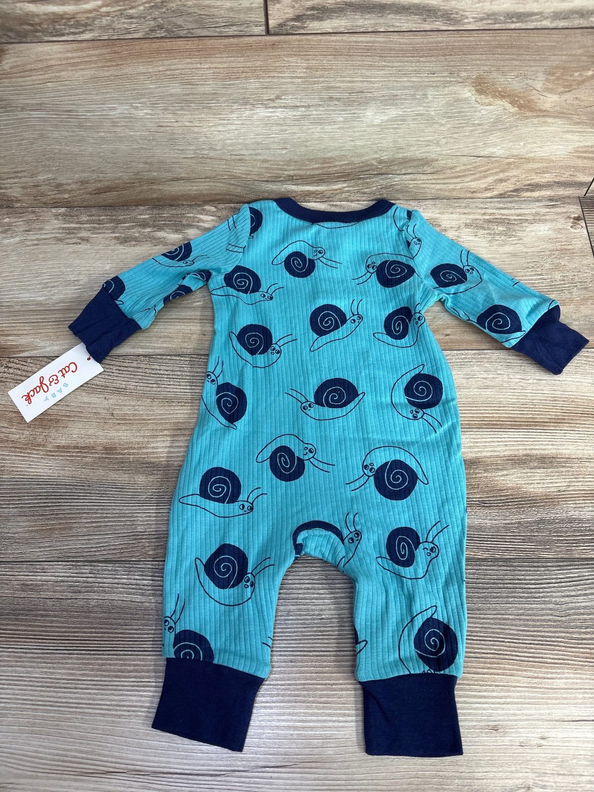 Blue baby onesie with navy snail print and navy cuffs on wooden background