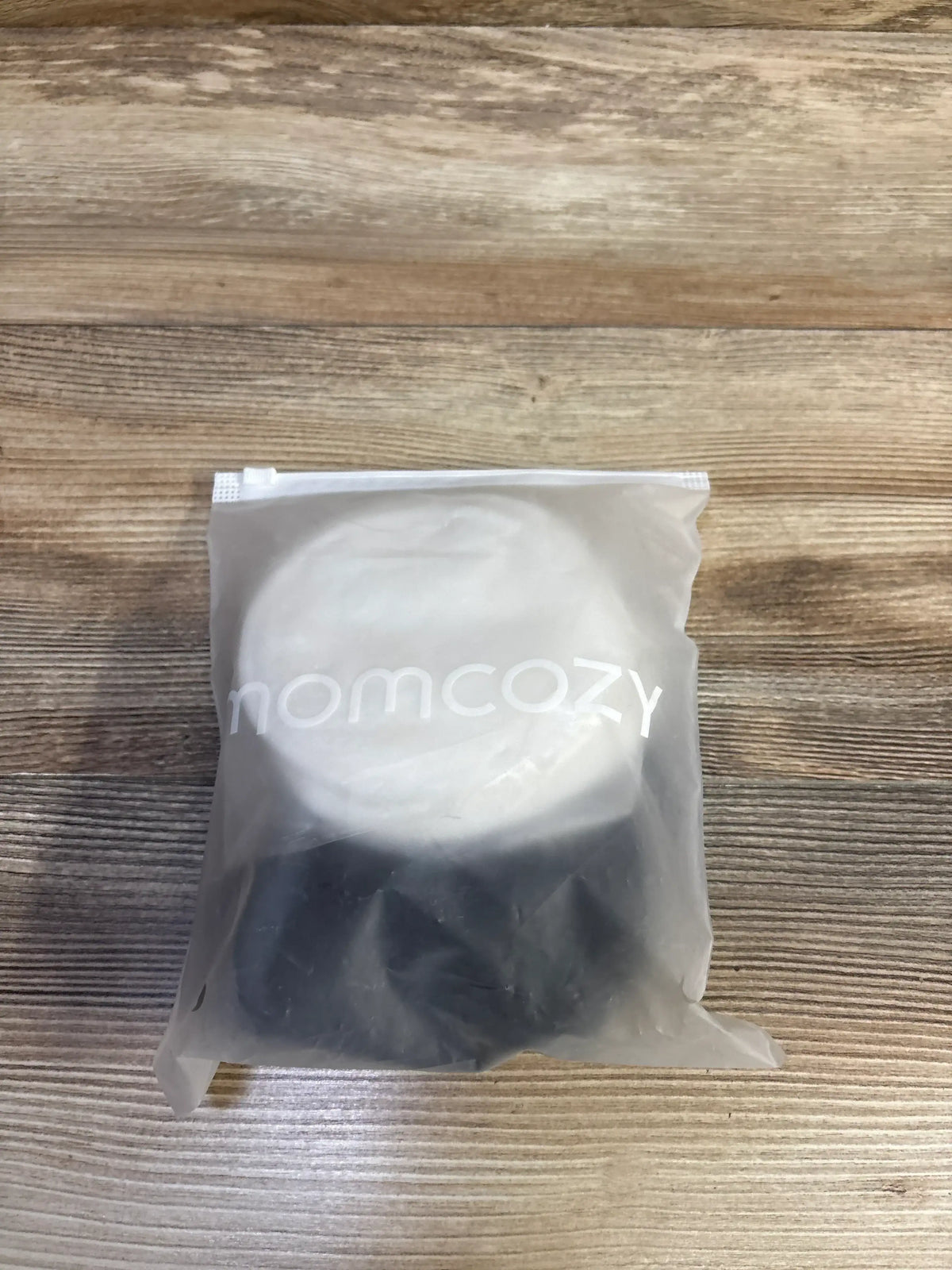 Top-down view of Momcozy hands-free pumping bra inserts in translucent bag showing white momcozy logo and black inserts on wood surface