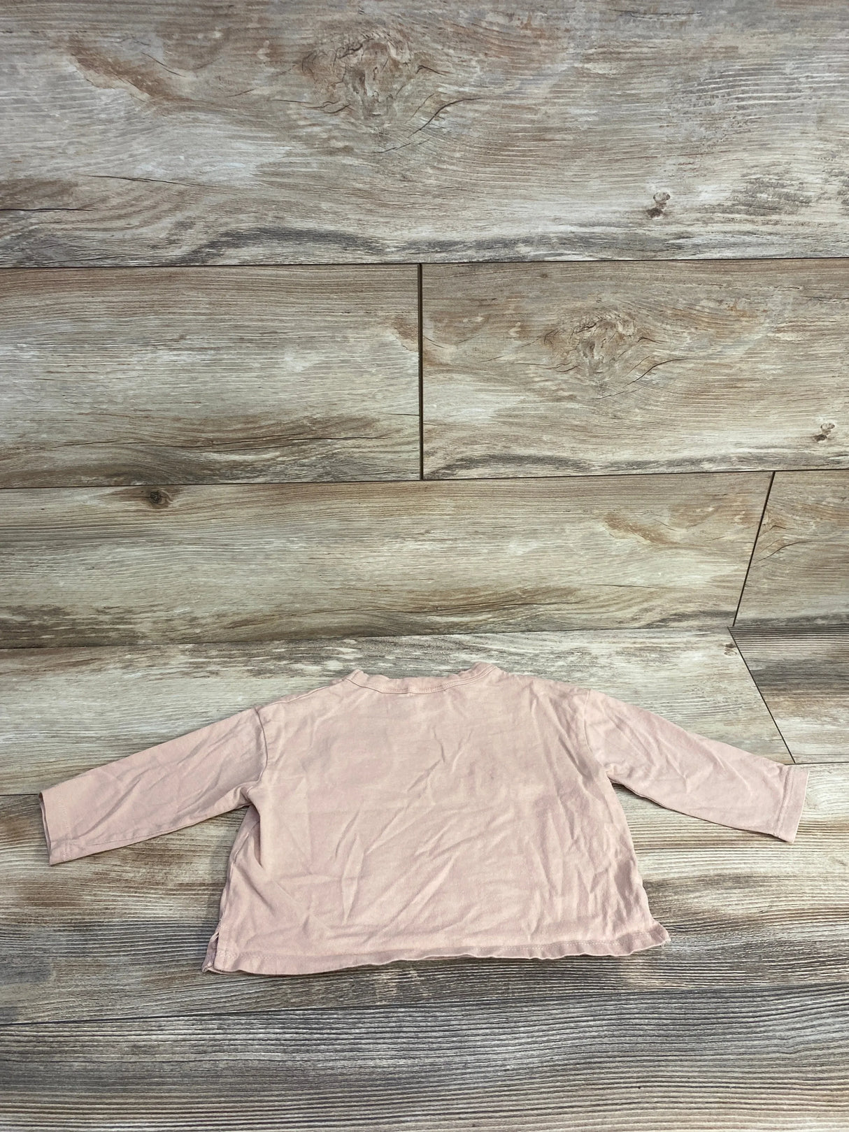 Long sleeve light pink baby shirt displayed on wood background, gently used kids clothing