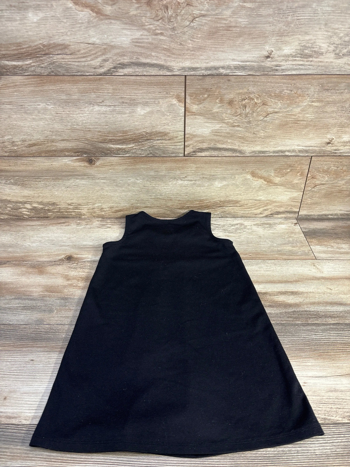 Front view of Children’s Place unicorn sleeveless ponte knit dress in black, laid flat on a wood-look floor
