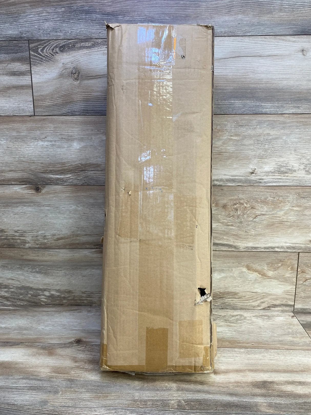 Top-down view of NEW Badminton Pro Set in long cardboard shipping box showing dent and tear on the side on wood floor background