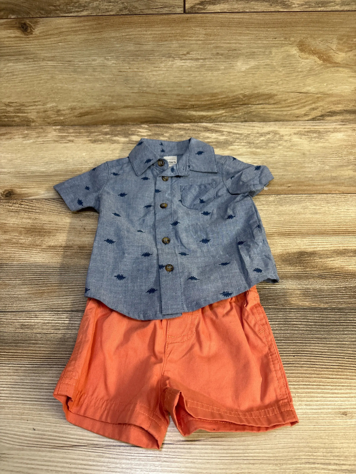 Flat lay of two-piece baby button-up set with blue printed shirt and orange elastic-waist shorts on wood background