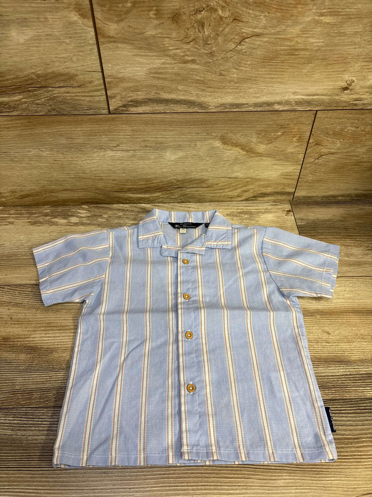 Front view of Ben Sherman toddler short-sleeve button-up shirt with vertical cream stripes on light blue and wooden buttons on wood background