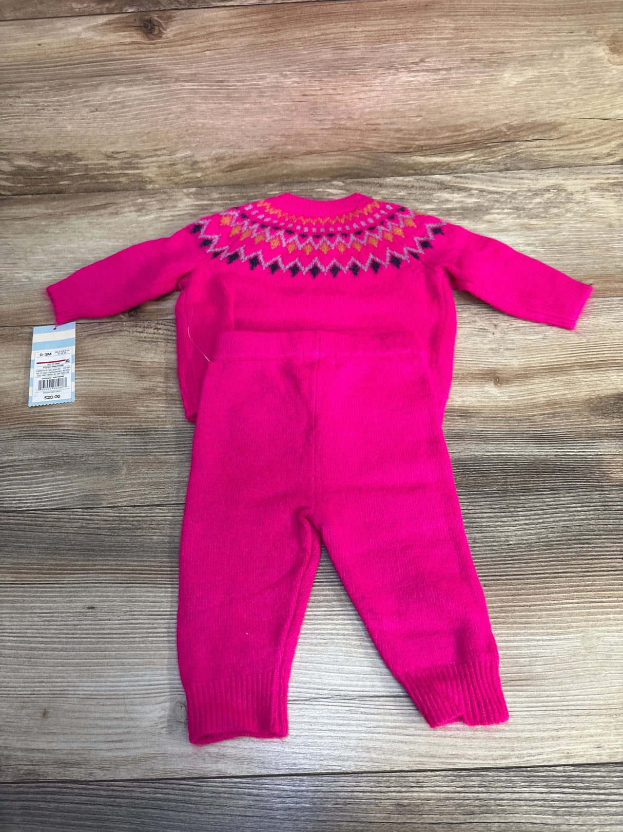 Bright pink knit baby outfit with long sleeves and geometric pattern, displayed on wood floor
