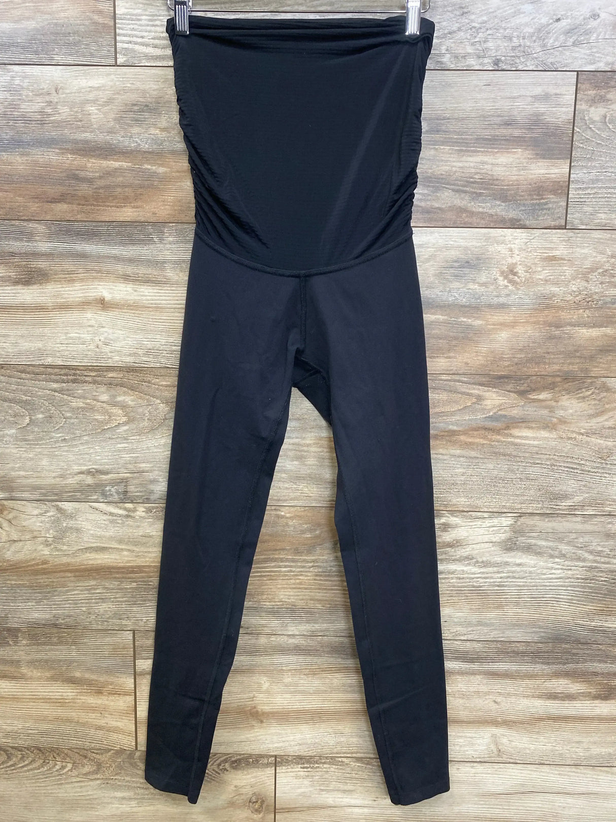 Front view of black maternity high-waist leggings with fold-over belly panel and side ruching on wood floor background