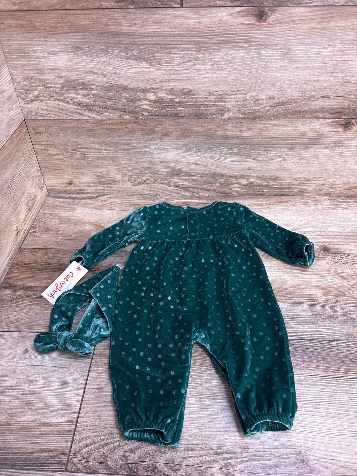 Green polka dot velvet baby romper with matching headband on wooden background