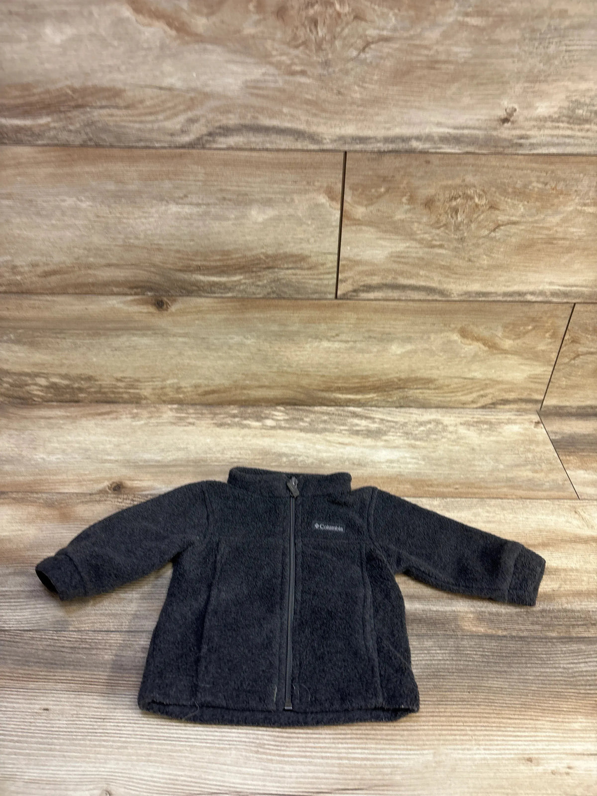Front view of toddler charcoal fleece zip jacket showcasing full-length zipper and Columbia logo on wood background