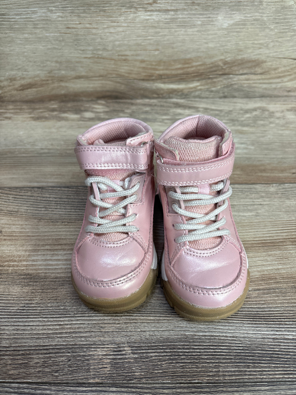 Pair of pink toddler sneakers with white laces and Velcro straps on wood floor