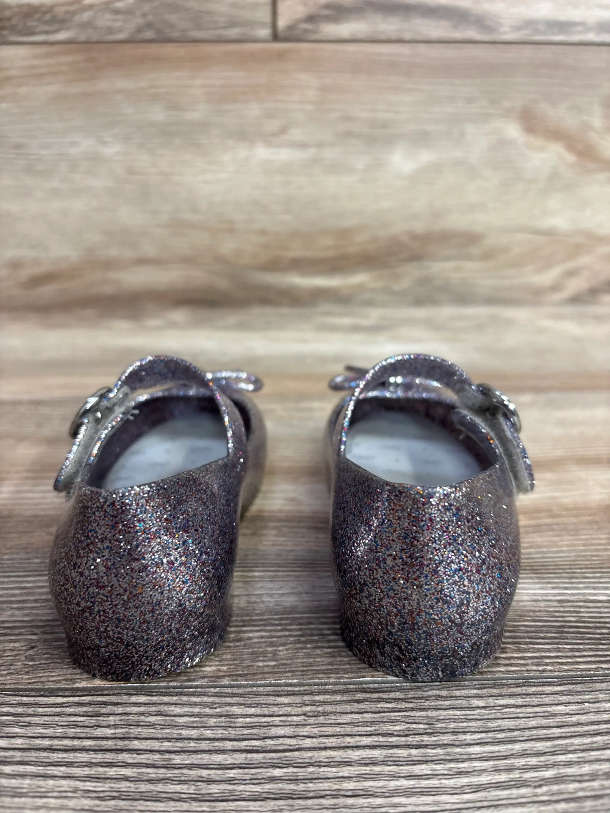 Pair of glittery dark purple toddler Mary Jane shoes on wooden surface, children's resale store item