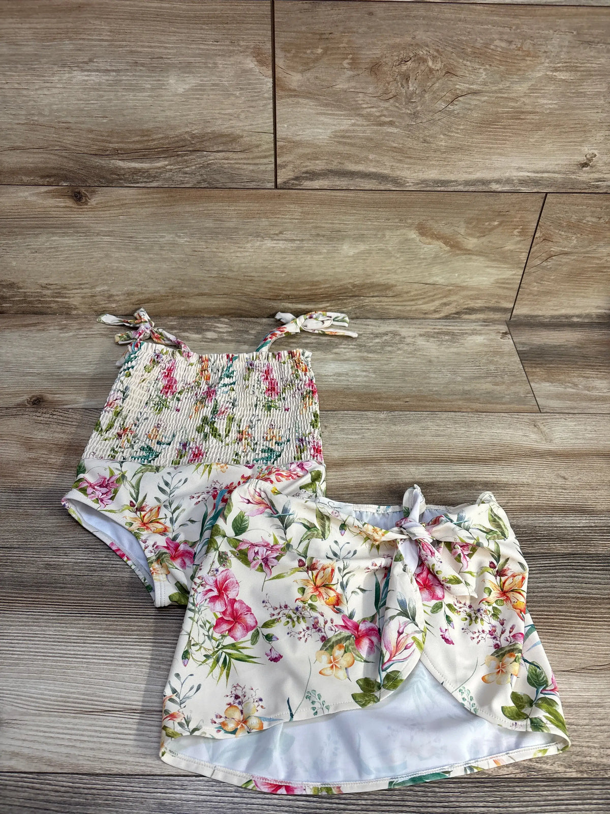 Top view of Jessica Simpson smocked swimsuit and skirt set showcasing floral print and tie straps on wood flooring