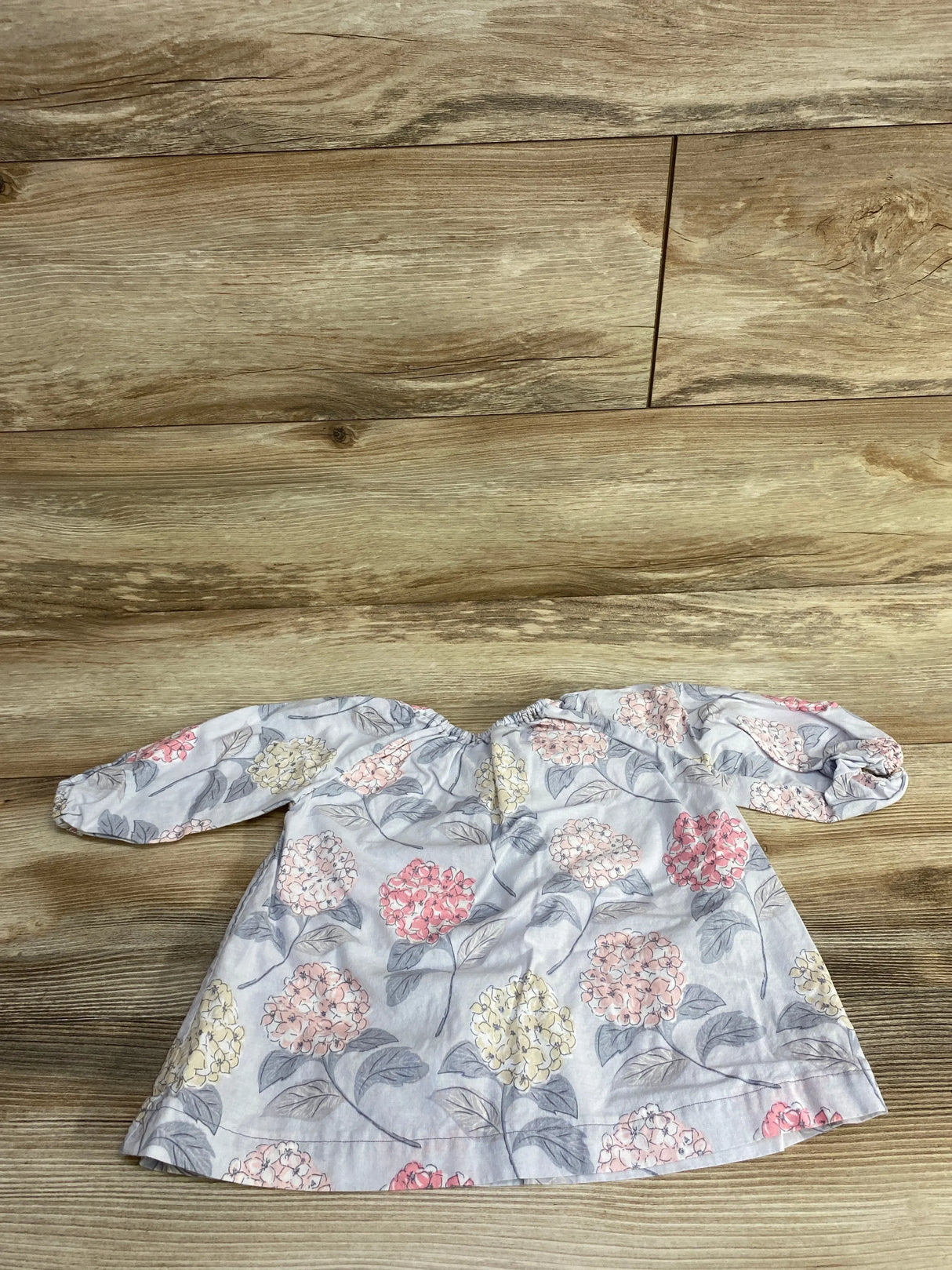 White baby blouse with pink, yellow, and gray floral pattern on wooden floor