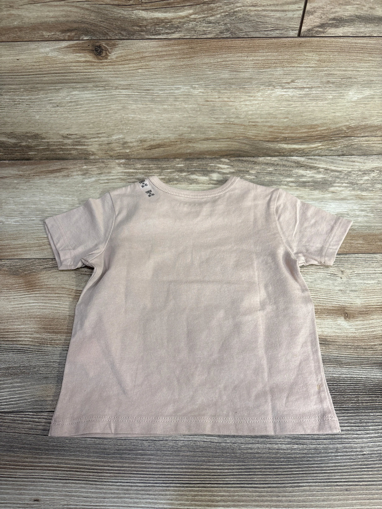 Light pink short-sleeve baby t-shirt on wood floor background at children's resale store