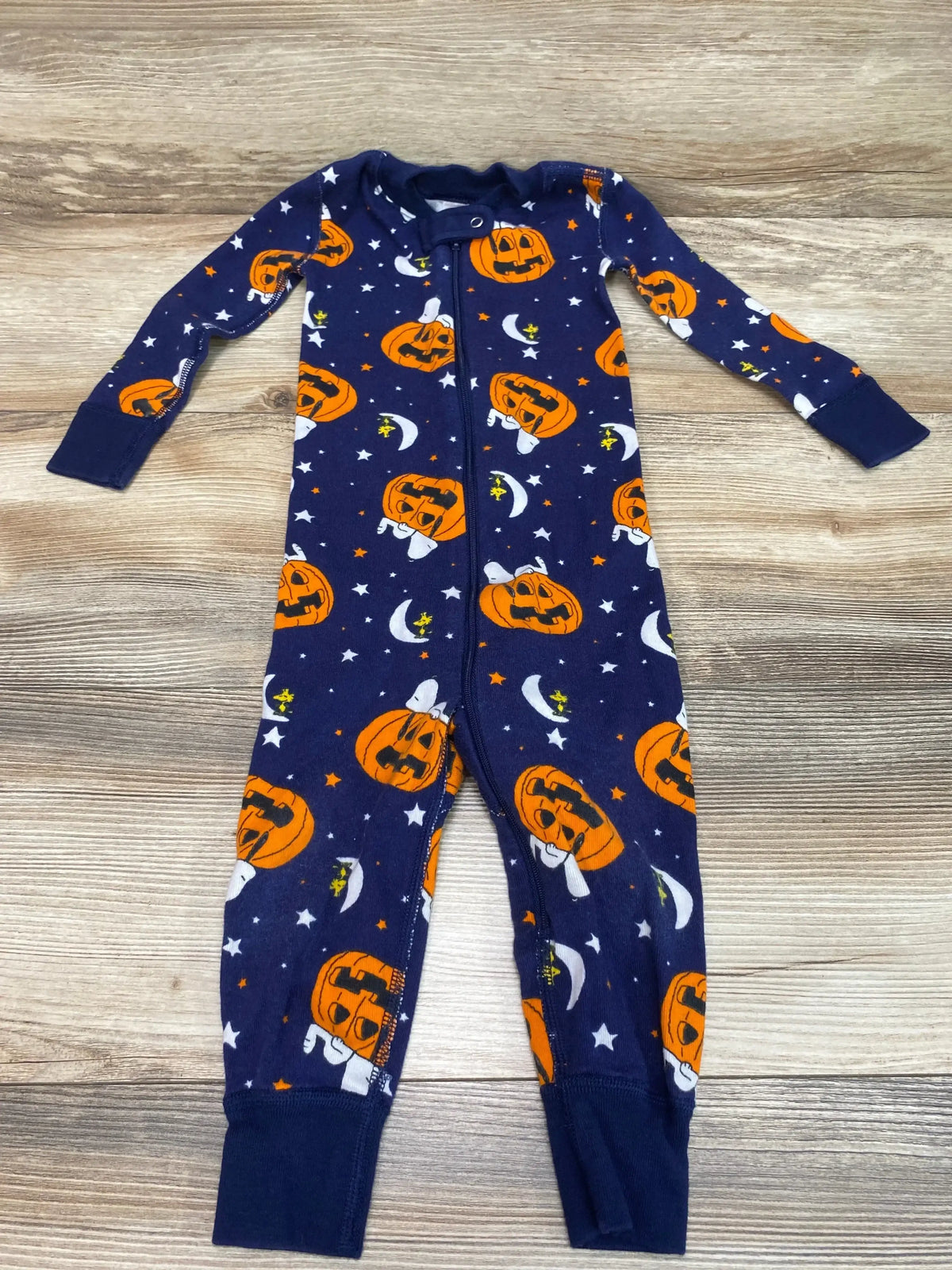 Flat lay of Hanna Andersson navy Peanuts Halloween zip sleeper (18-24 months) showing front zipper and orange pumpkin and moon print on wood background