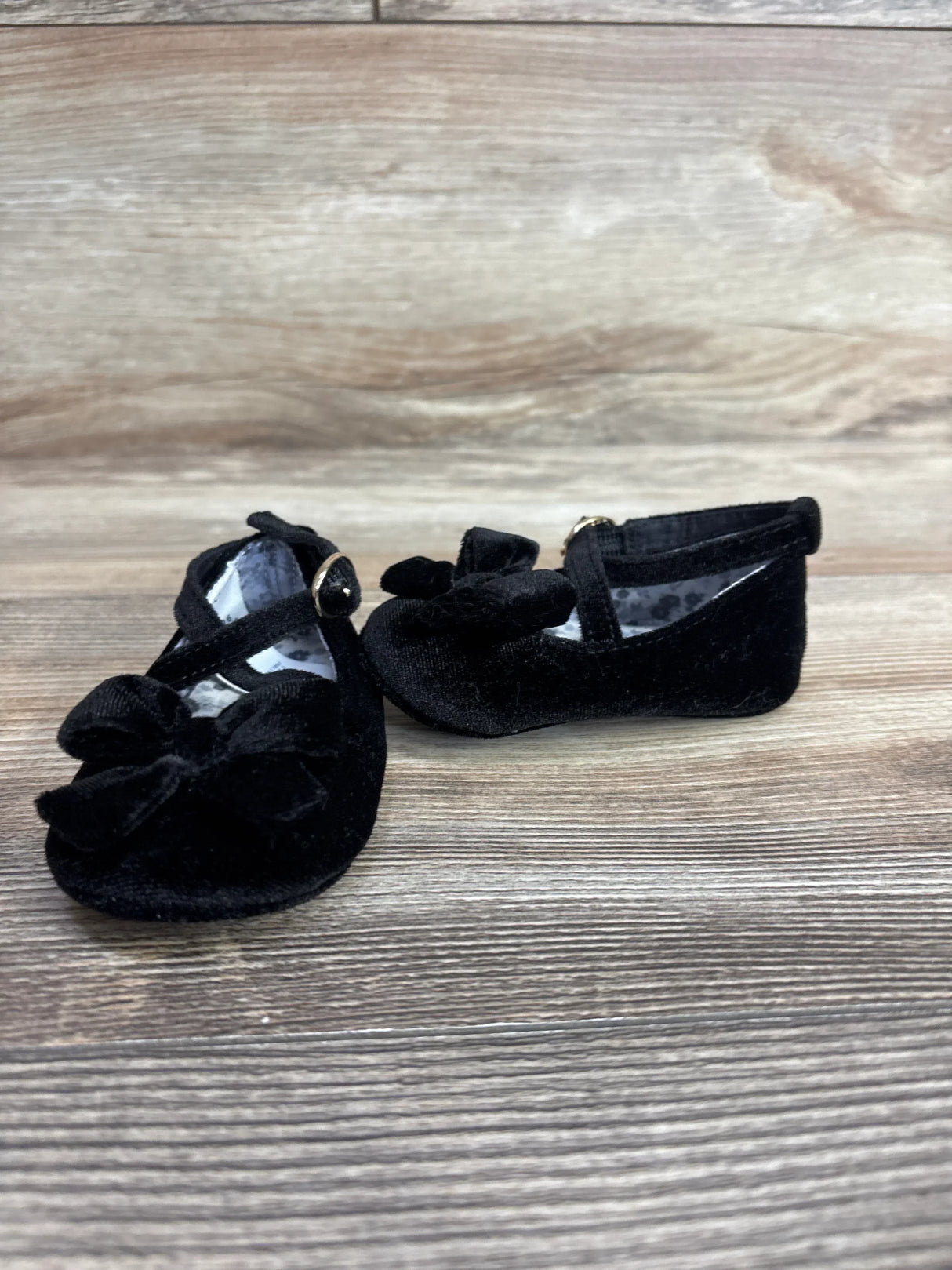 Black velvet baby shoes with bows and ankle straps on wood background