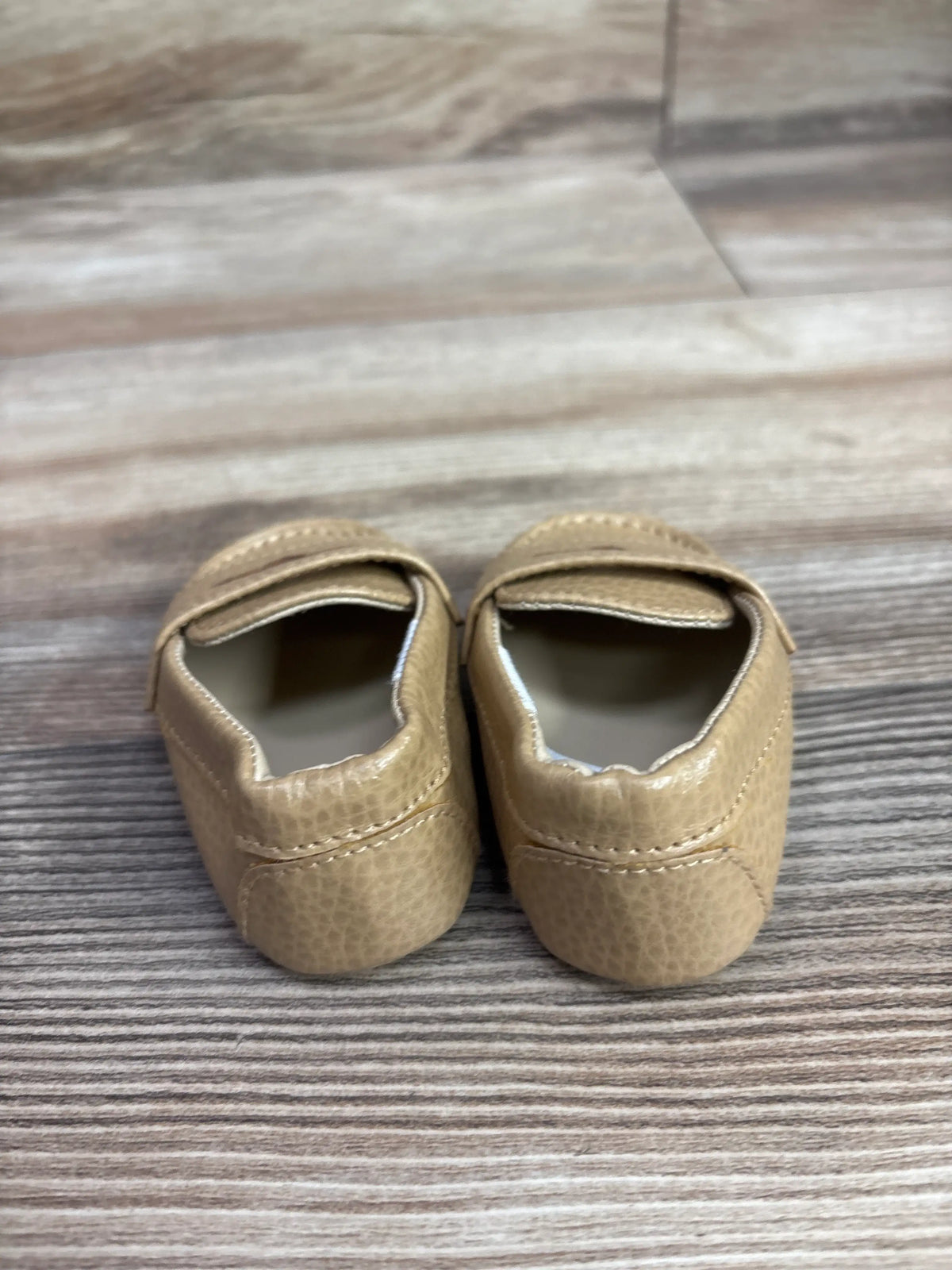 Pair of tan Janie & Jack penny loafer shoes for infants on a wooden surface
