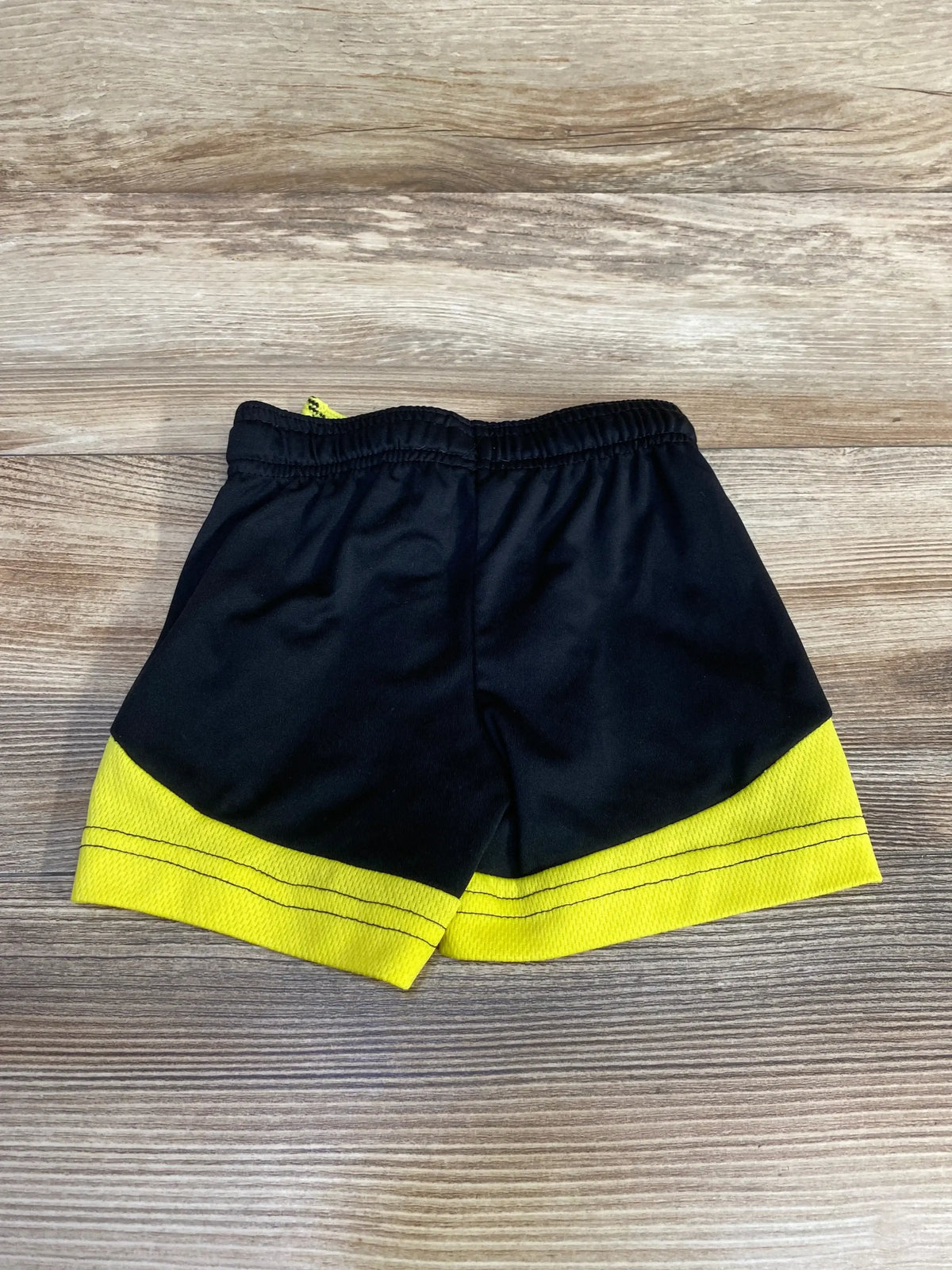 Front view of black Jumping Beans baby shorts showing yellow hem stripes and elastic drawstring waist on wood background
