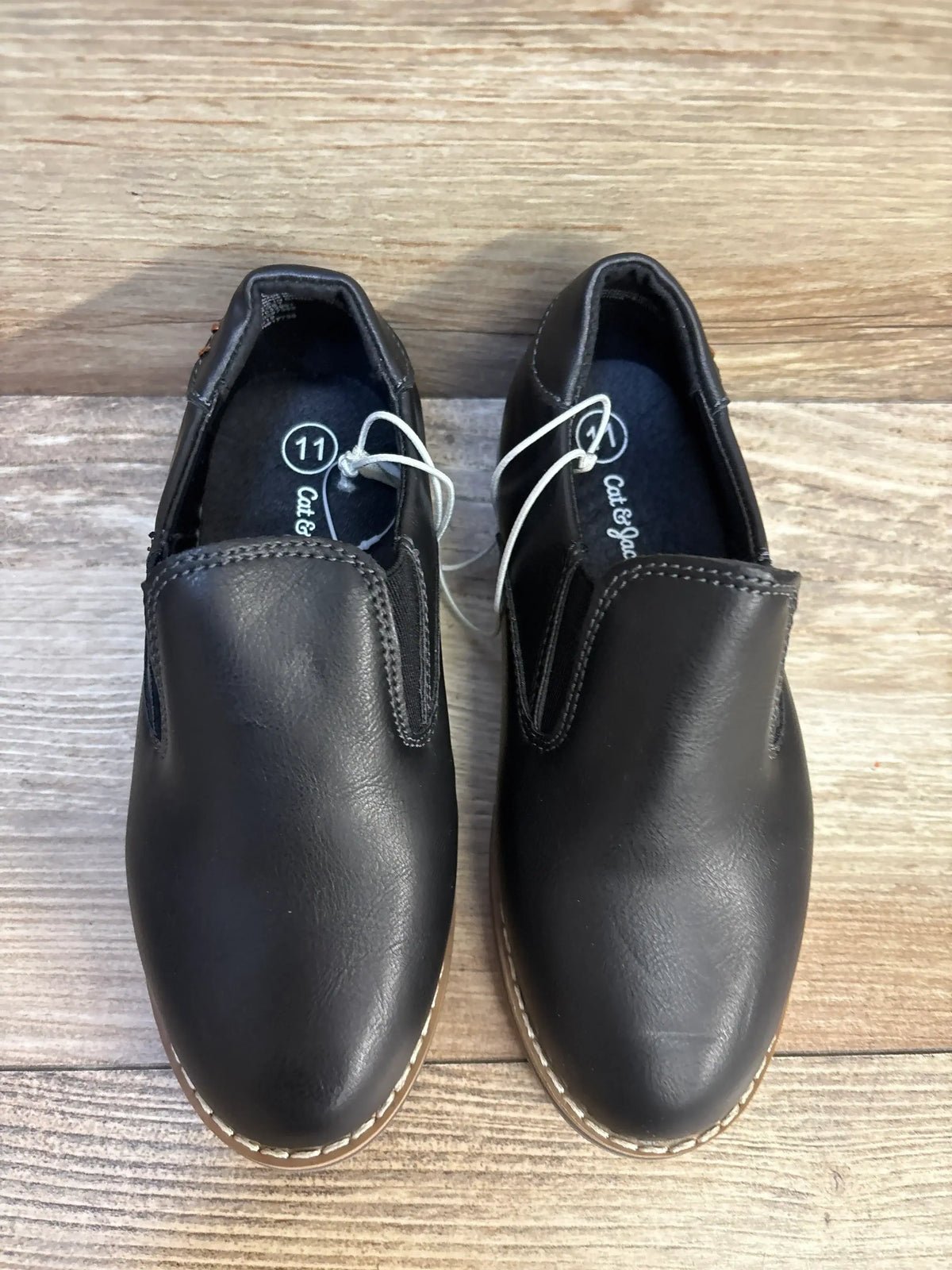 Black slip-on toddler dress shoes size 11 with stitching detail on wood floor