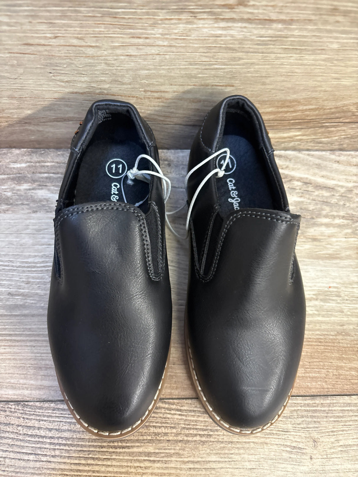 Black slip-on toddler dress shoes size 11 with stitching detail on wood floor