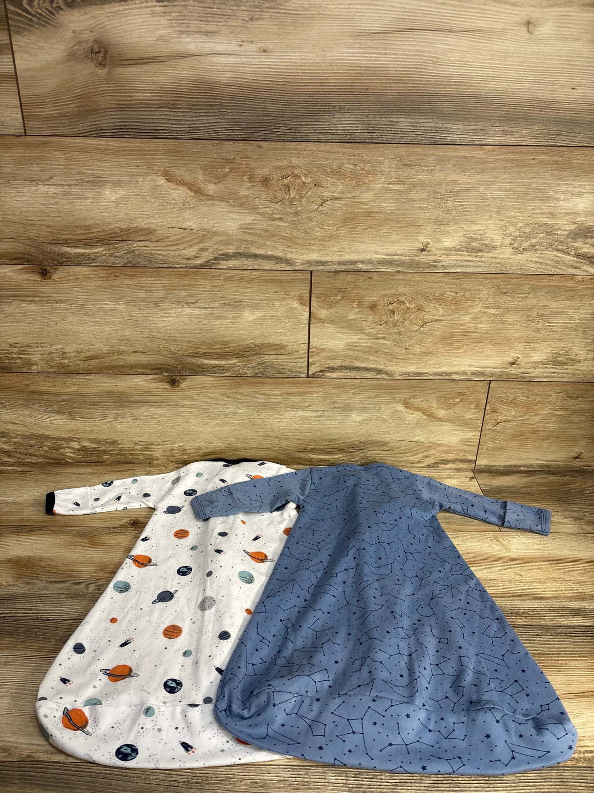 Two baby sleep sacks with space-themed and constellation prints on wooden floor
