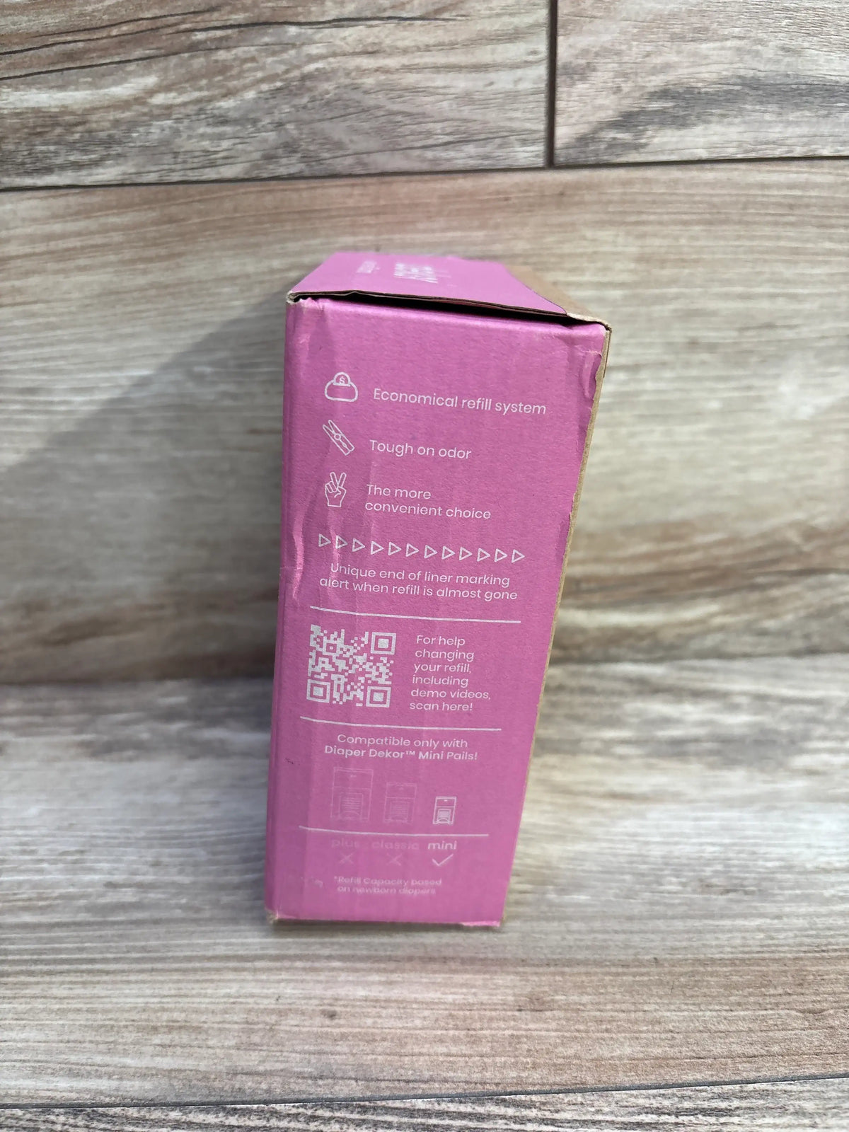 Side view of Diaper Dekor Eko Mini refill 2-pack box showing feature list, QR code, and compatibility note on wood background