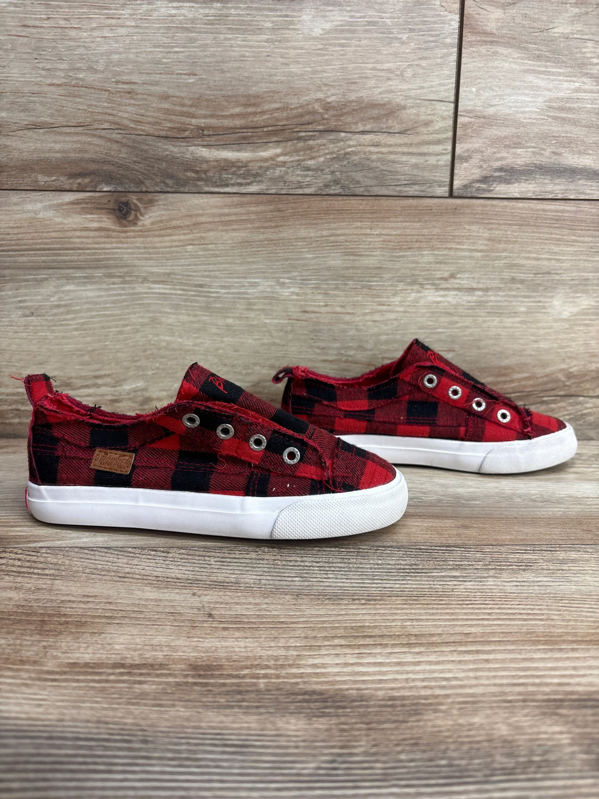 Red and black plaid slip-on kids sneakers with white soles on wooden floor background