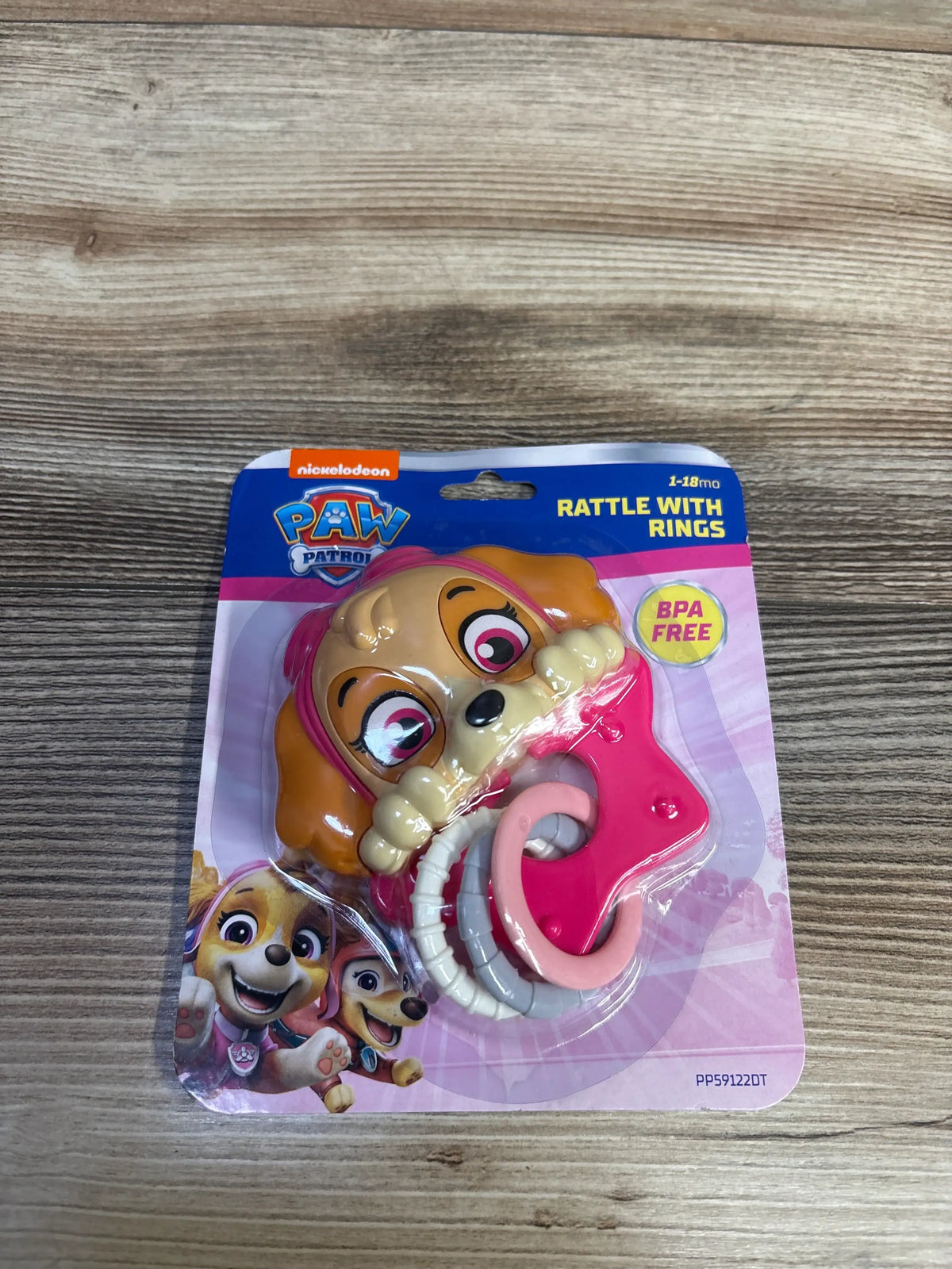 Front view of Nickelodeon PAW Patrol rattle with rings showcasing pink and white rings and puppy character packaging on a wooden table