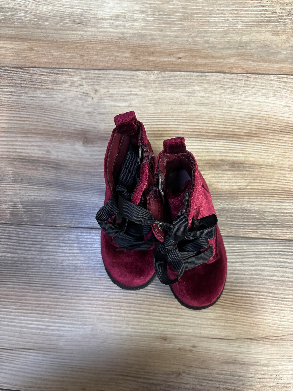 Top view of Cat and Jack velvet toddler ankle boots in burgundy showing black ribbon laces and side zipper on wood floor