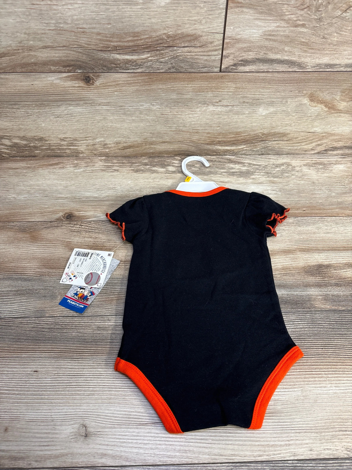 Black baby onesie with orange trim on wood background, tags attached, on hanger