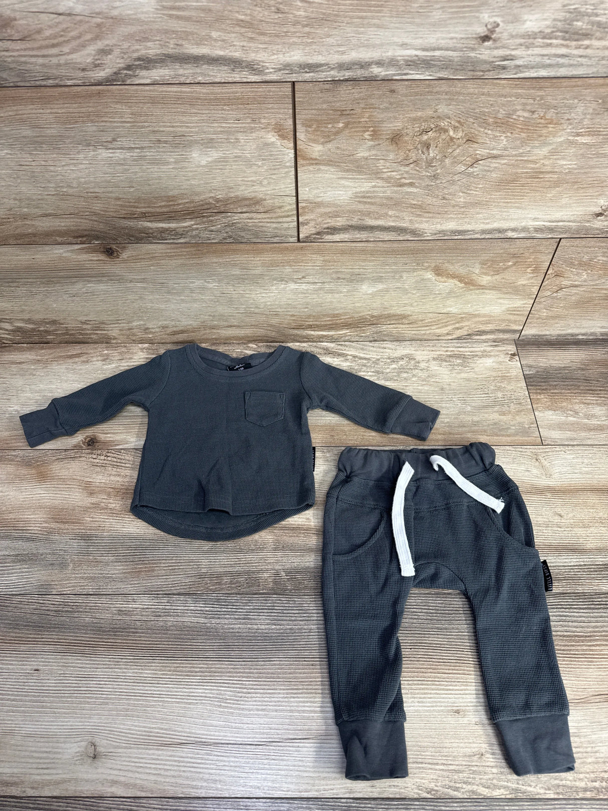 Dark gray long-sleeve baby shirt with pocket and matching pants with white drawstring on wooden floor
