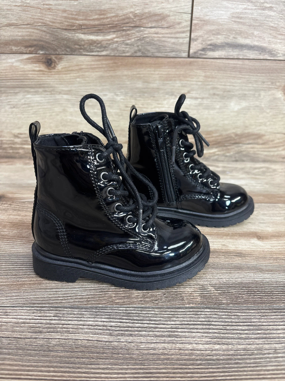 Shiny black toddler lace-up combat boots with side zipper on wood floor