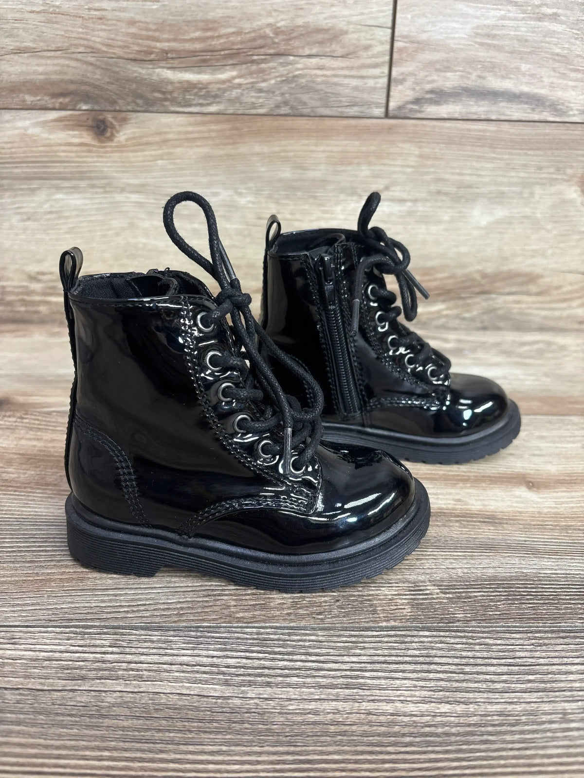 Shiny black toddler lace-up combat boots with side zipper on wood floor