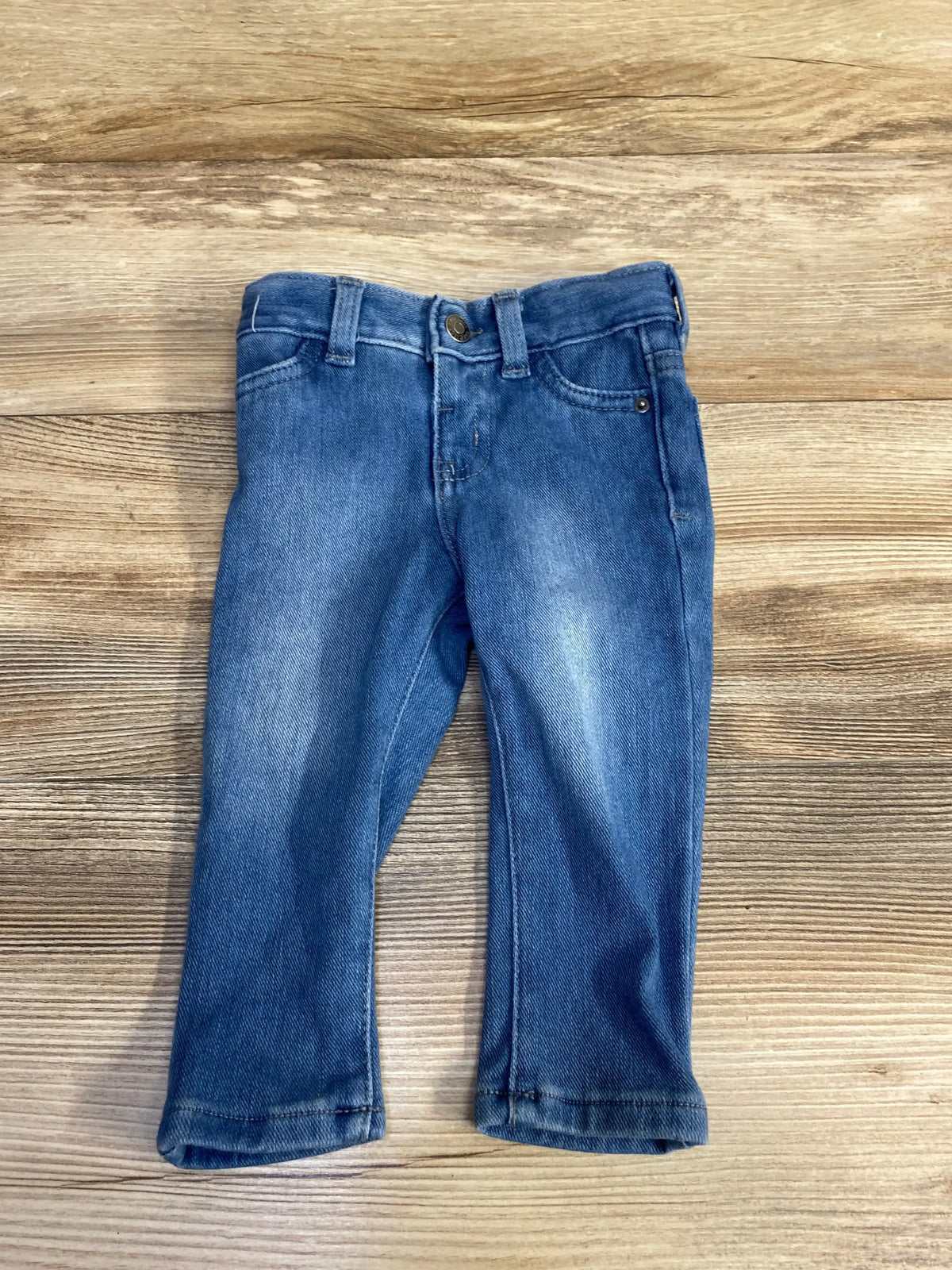 Front view of Cat and Jack blue jeggings size 12m showing button waist, faux pockets and faded thighs on wood background
