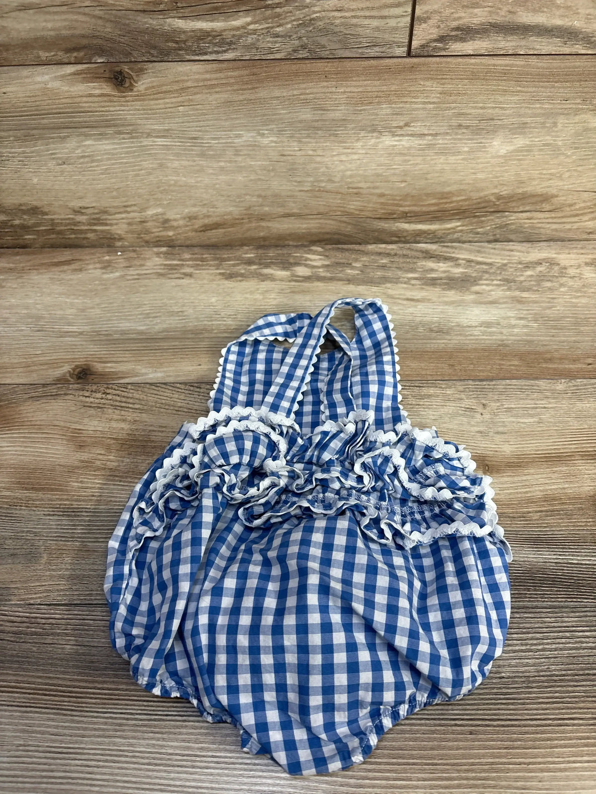 Top view of blue gingham ruffle bubble romper showing ruffled chest and crisscross straps on wood background