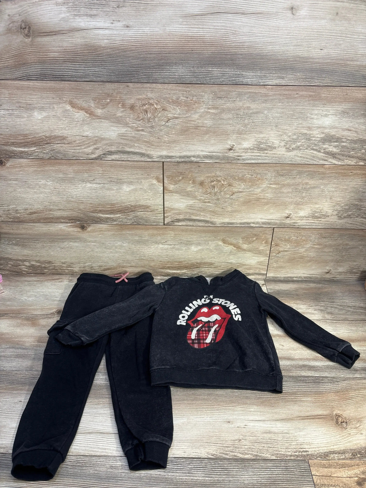 Flat lay of grey toddler Rolling Stones sweatshirt and joggers showing red tongue logo with plaid detail on wood floor