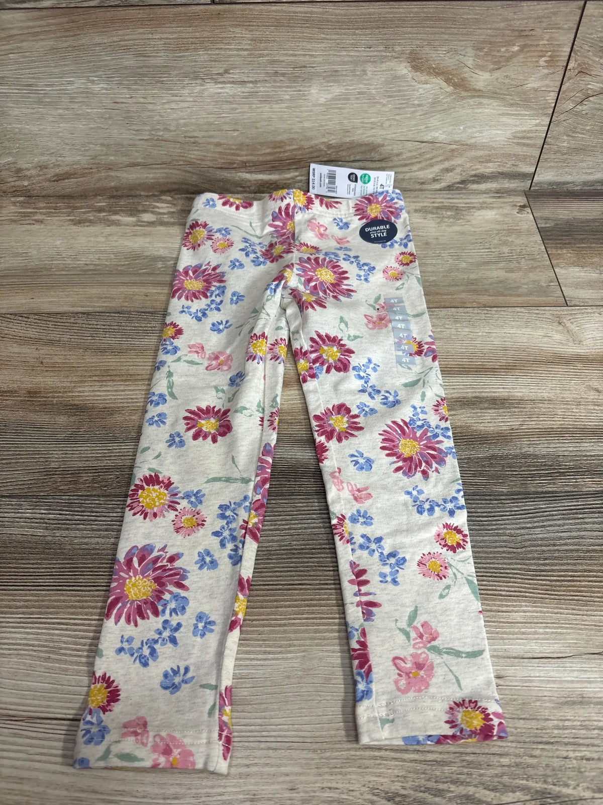Front view of OshKosh beige floral leggings size 4T with waistband and pink and blue daisy print on wood floor
