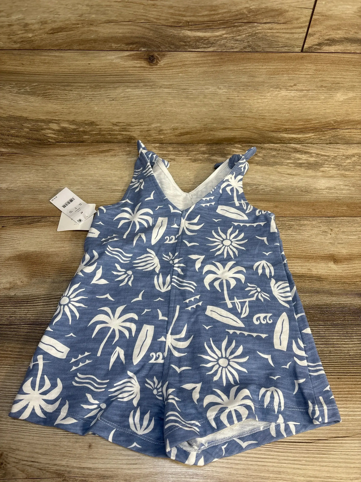 Blue toddler romper with white tropical print, palm trees, and surfboards on wood background