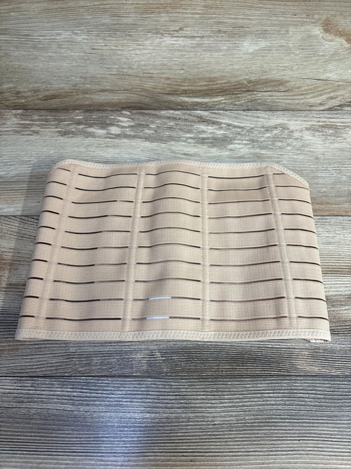 Beige elastic waist support belt with horizontal slits on wooden surface
